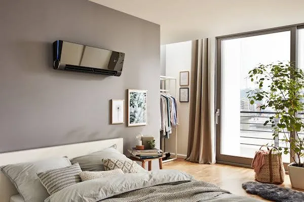 Modernes Wand-Klimagerät über einem Bett in einem stilvoll eingerichteten Schlafzimmer mit Balkonzugang